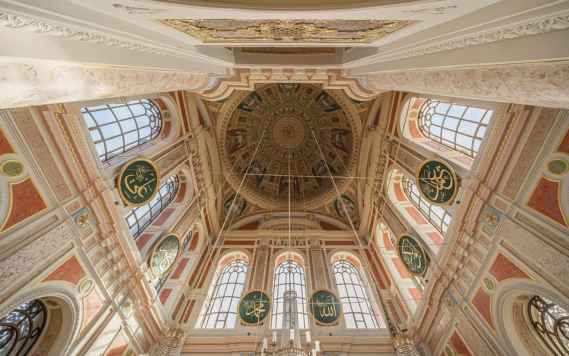 Looking up into the dome of the Ortaköy Mosque, with tall arched windows and painted pendentives