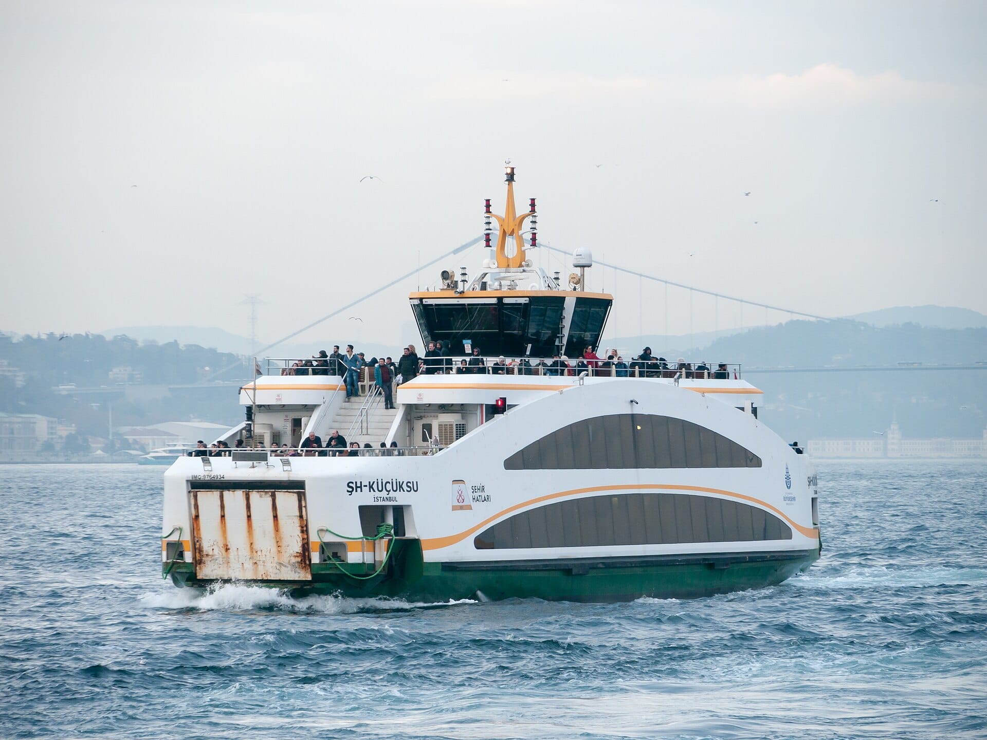 A white commuter ferry crossing the Bosphorus with passengers on deck